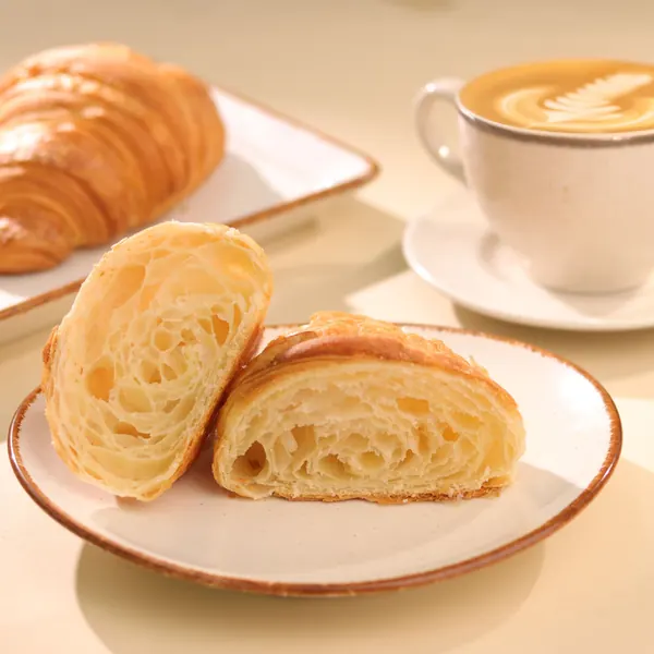 A butter croissant cut open beside a cappuccino